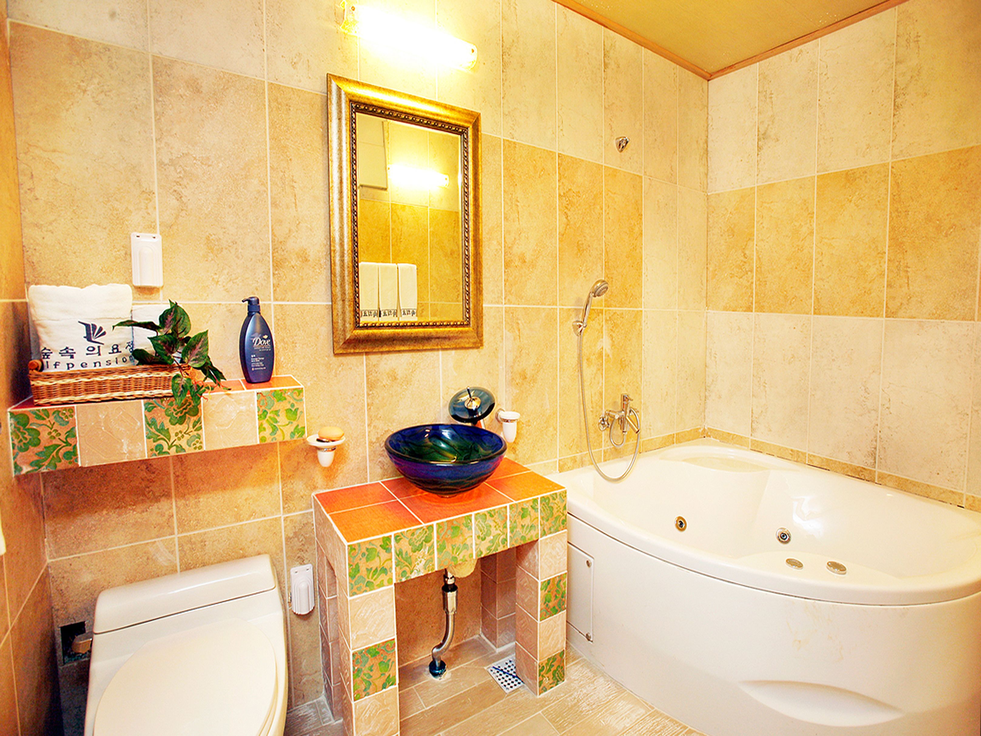 A bathroom with a bathtub, a sink with a decorative bowl, a mirror, and a toilet.
