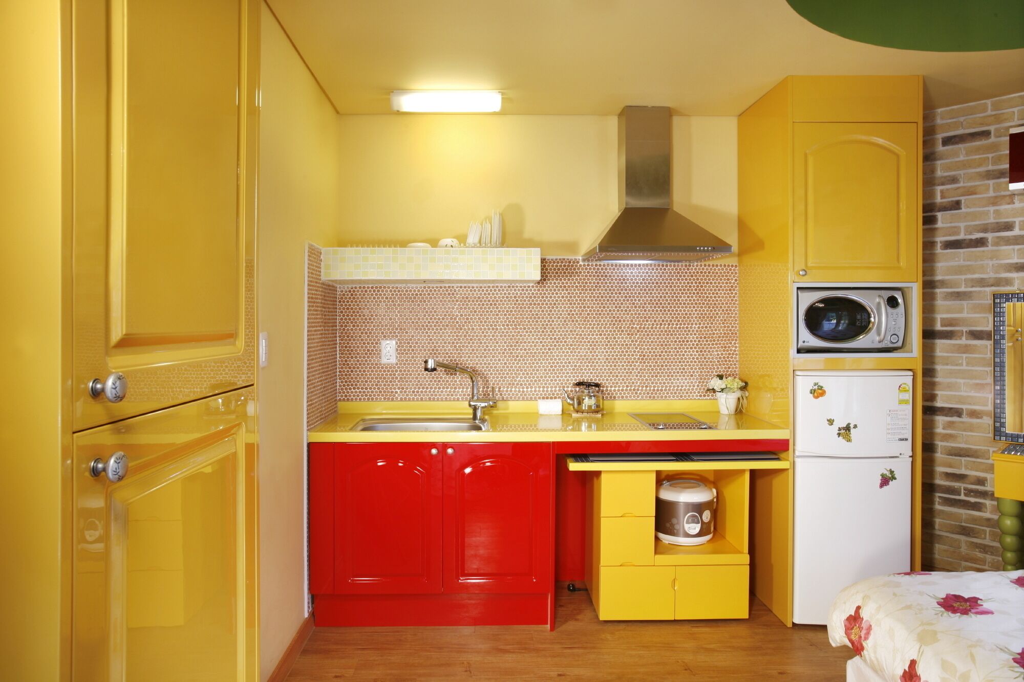 A compact kitchen with yellow cabinets, a red countertop, a sink, a microwave, and a refrigerator.