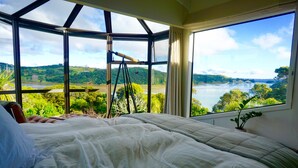 A bedroom with a large window offering a view of a lake and hills.