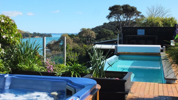 A hot tub and a small pool on a wooden deck with a view of the sea and hills.