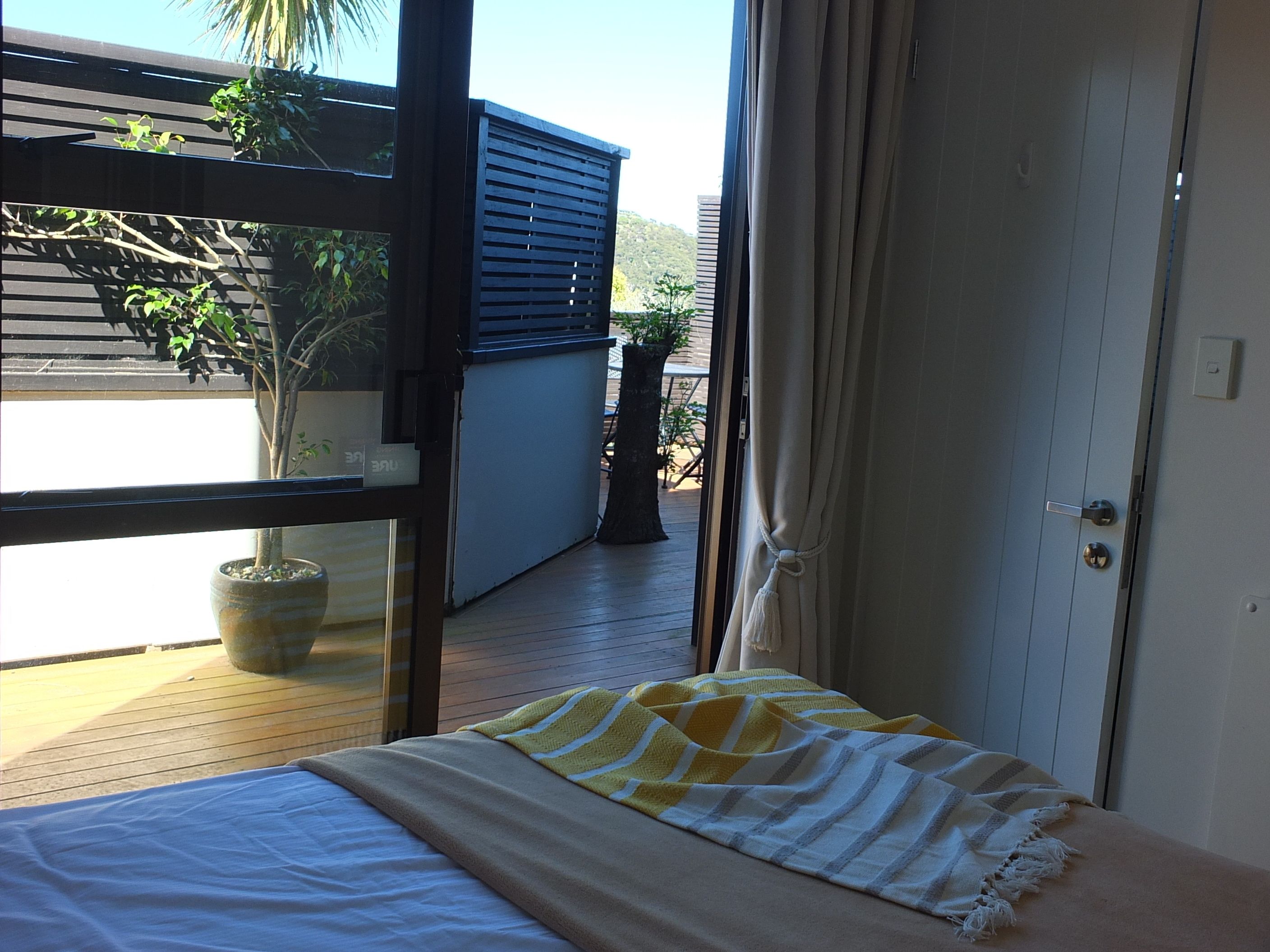 A bedroom with a bed, a window, and a view of the outside balcony.