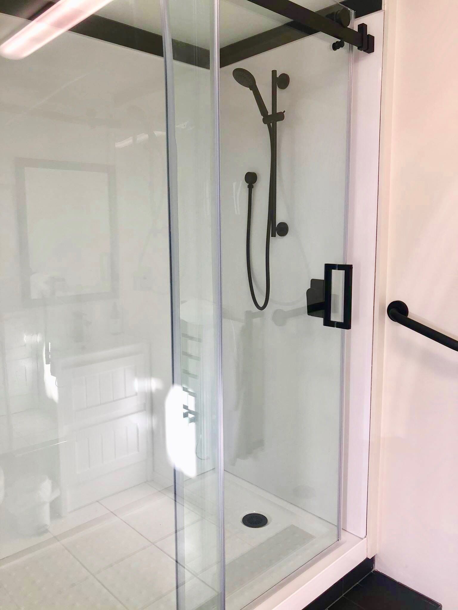 A glass-enclosed shower area with a control panel and a handheld showerhead.