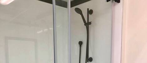 A glass-enclosed shower area with a control panel and a handheld showerhead.