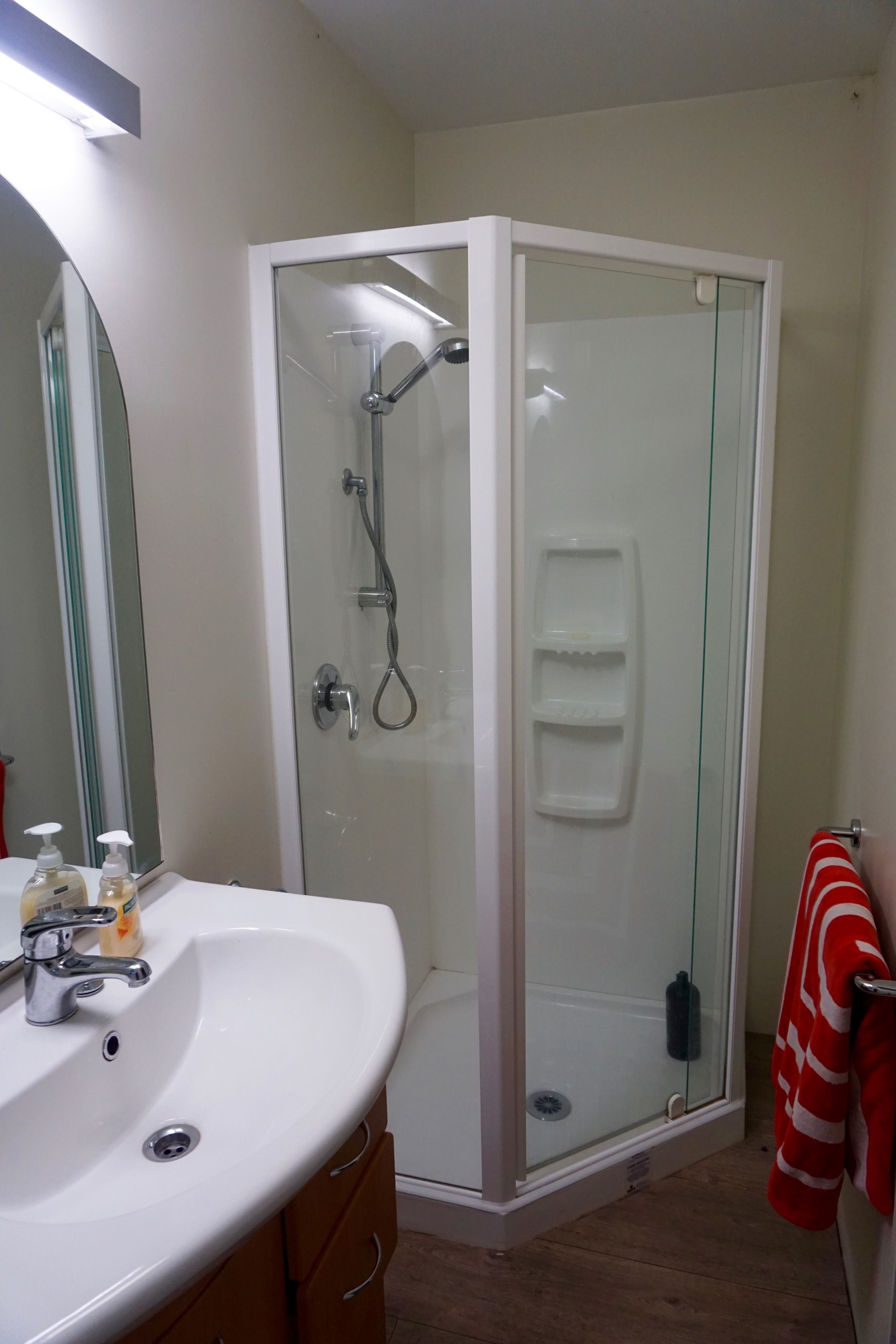 A bathroom with a glass-enclosed shower, a white sink with soap dispensers, and a red towel hanging on a rack.
