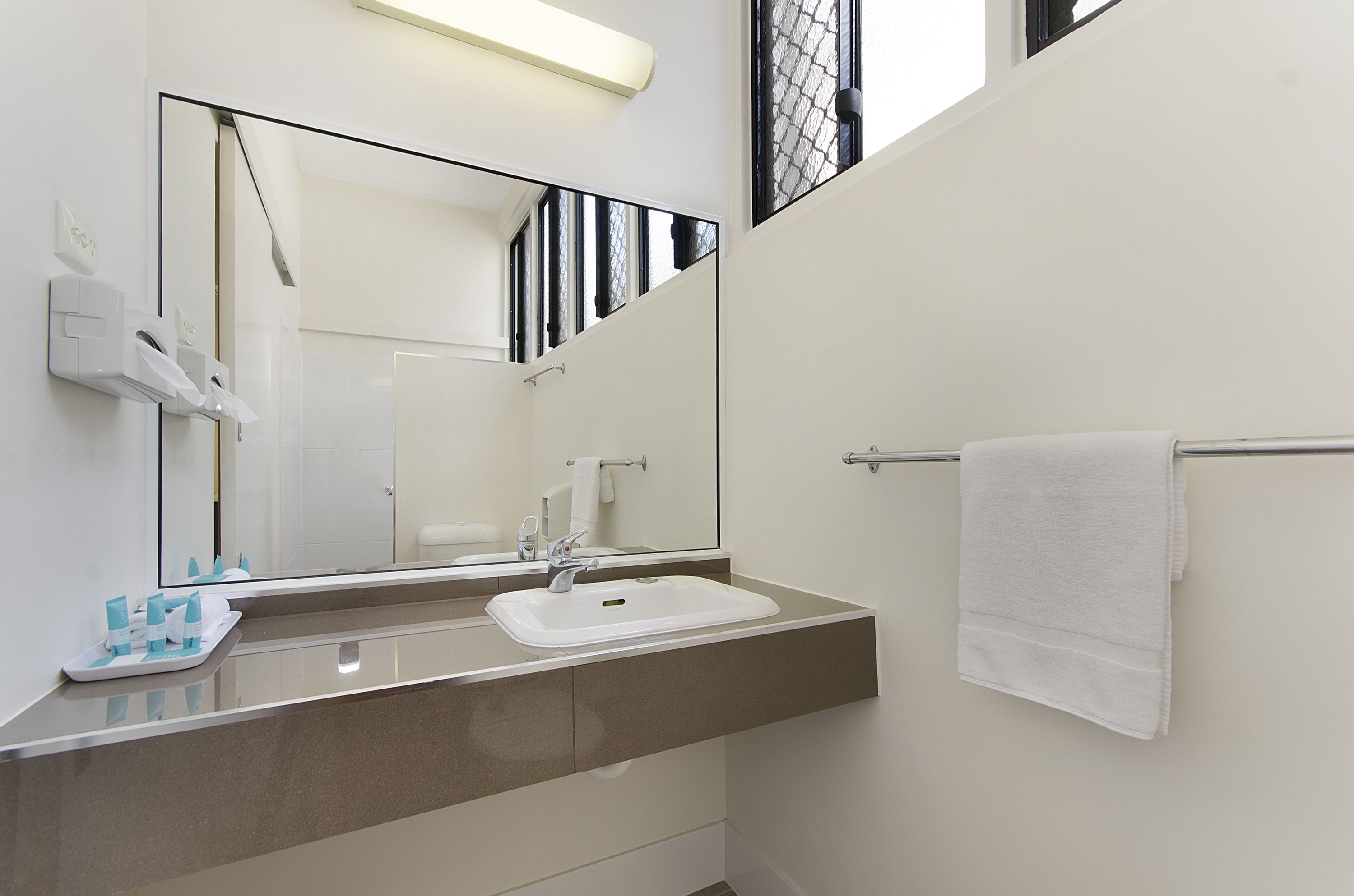 Un baño moderno con un espejo grande, un lavabo blanco y un perchero para toallas.
