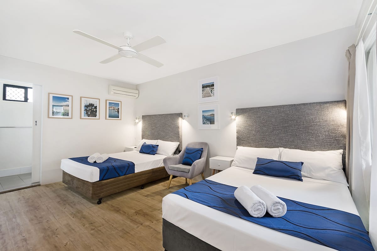 Une chambre d’hôtel avec deux lits, un ventilateur de plafond et des tableaux encadrés accrochés au mur.