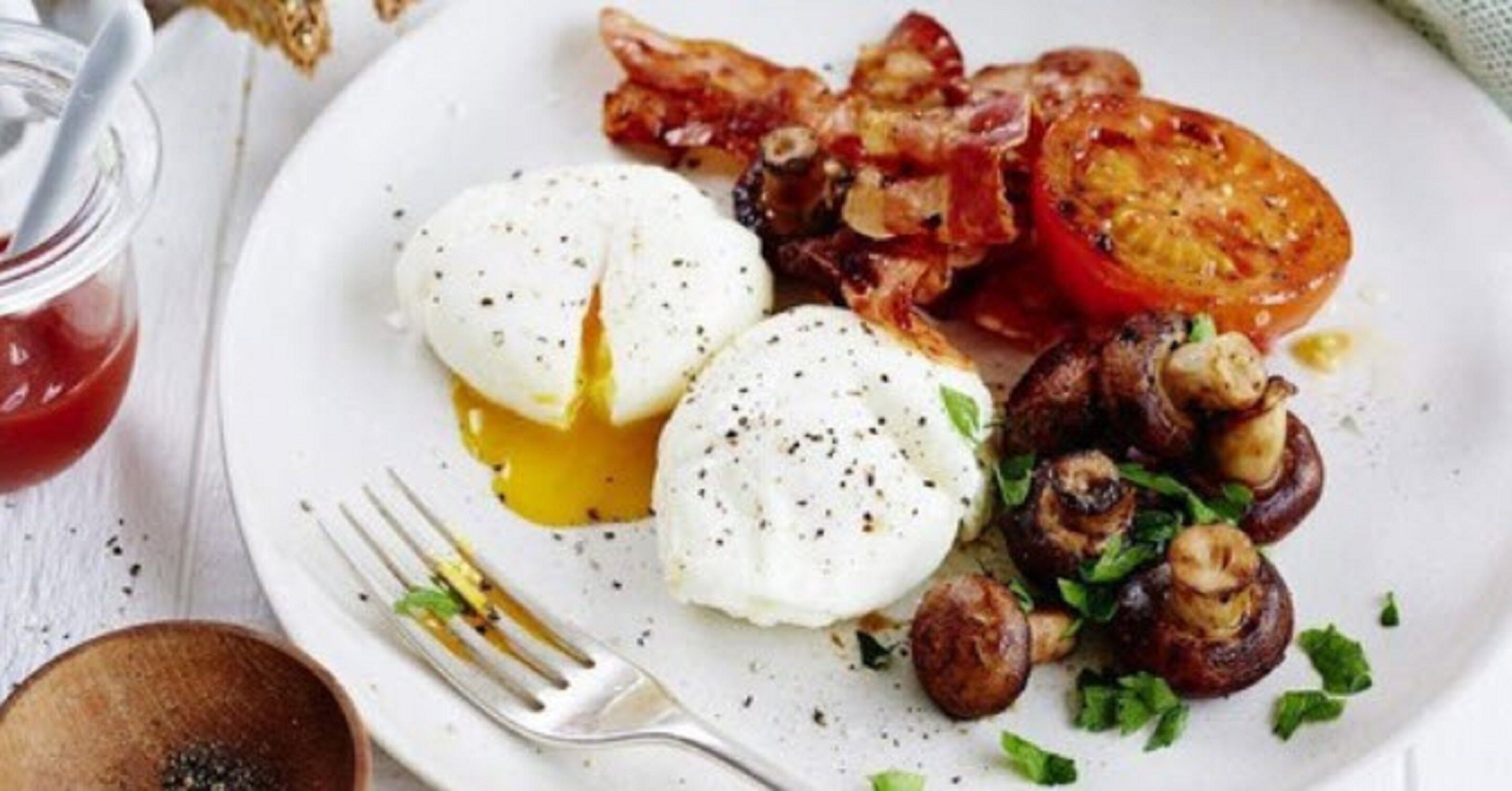 Un plato con huevos, tocino, champiñones y una rodaja de tomate.