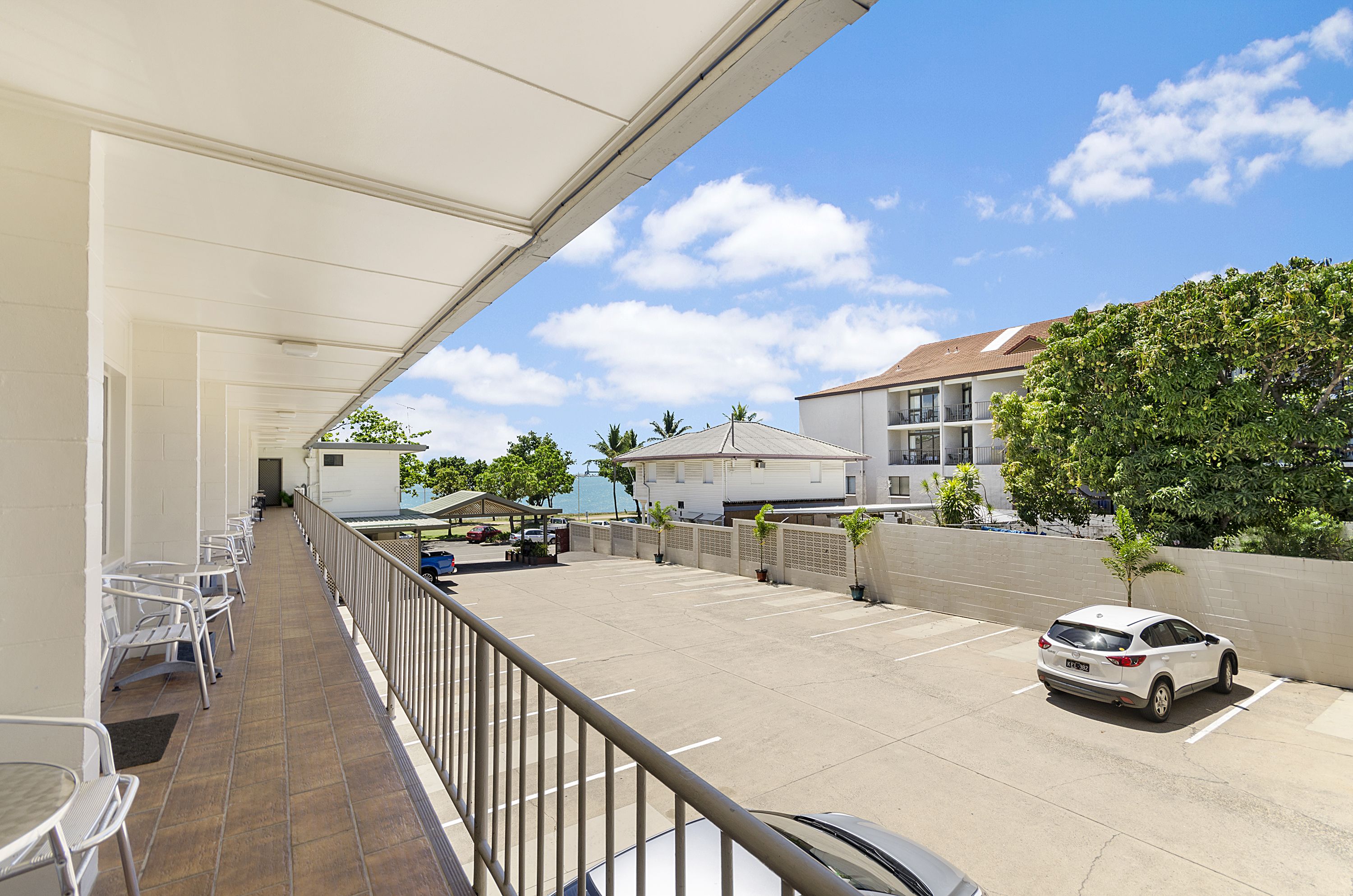 A covered outdoor area with a row of white chairs, a parking lot, and a white car parked near the building.