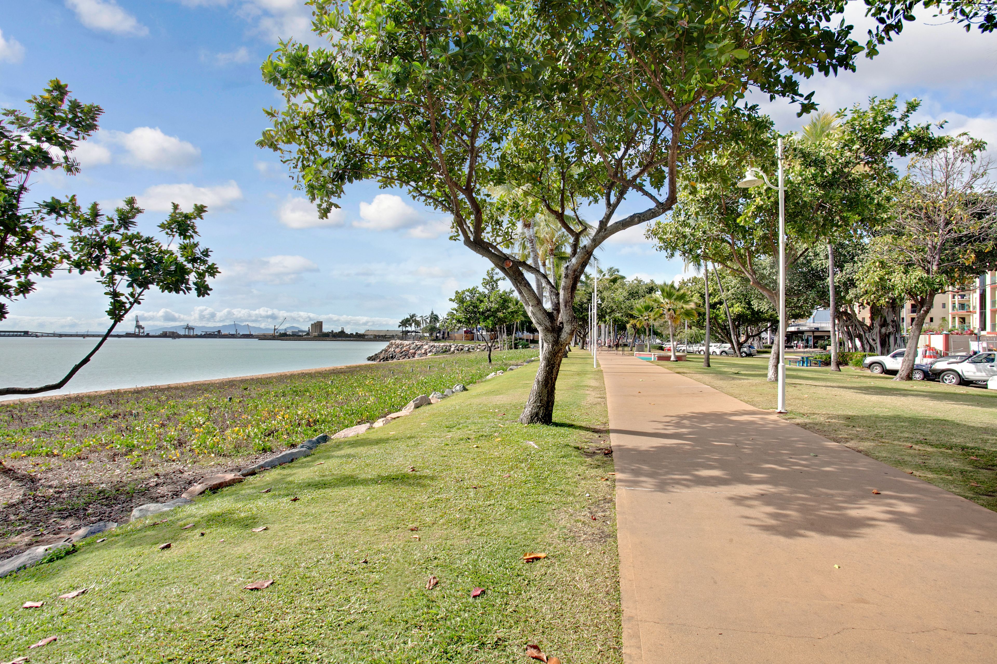 A park with a paved walkway, grassy areas, and trees.