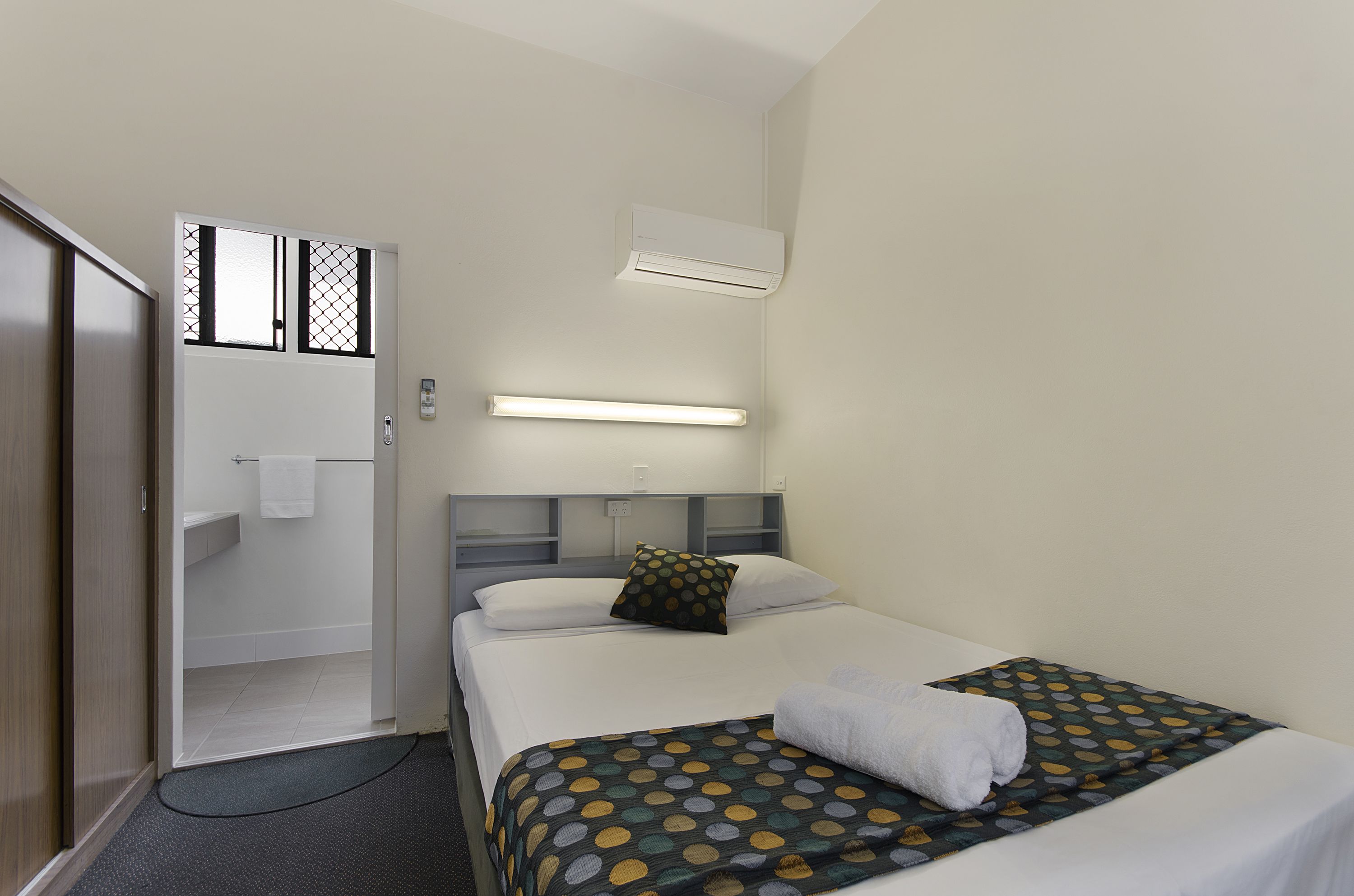 Habitación de hotel con cama, mesita de noche, armario, baño con inodoro y lavamanos, y ventana con vista al exterior.