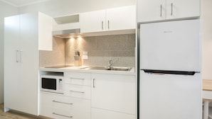 A modern kitchen with white cabinetry, a stainless steel sink, and a built-in microwave. - Beach House Motel (North Ward)