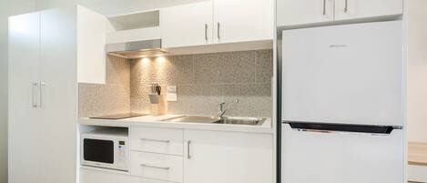 Una cocina moderna con armarios blancos, un lavamanos de acero inoxidable y un microondas integrado.