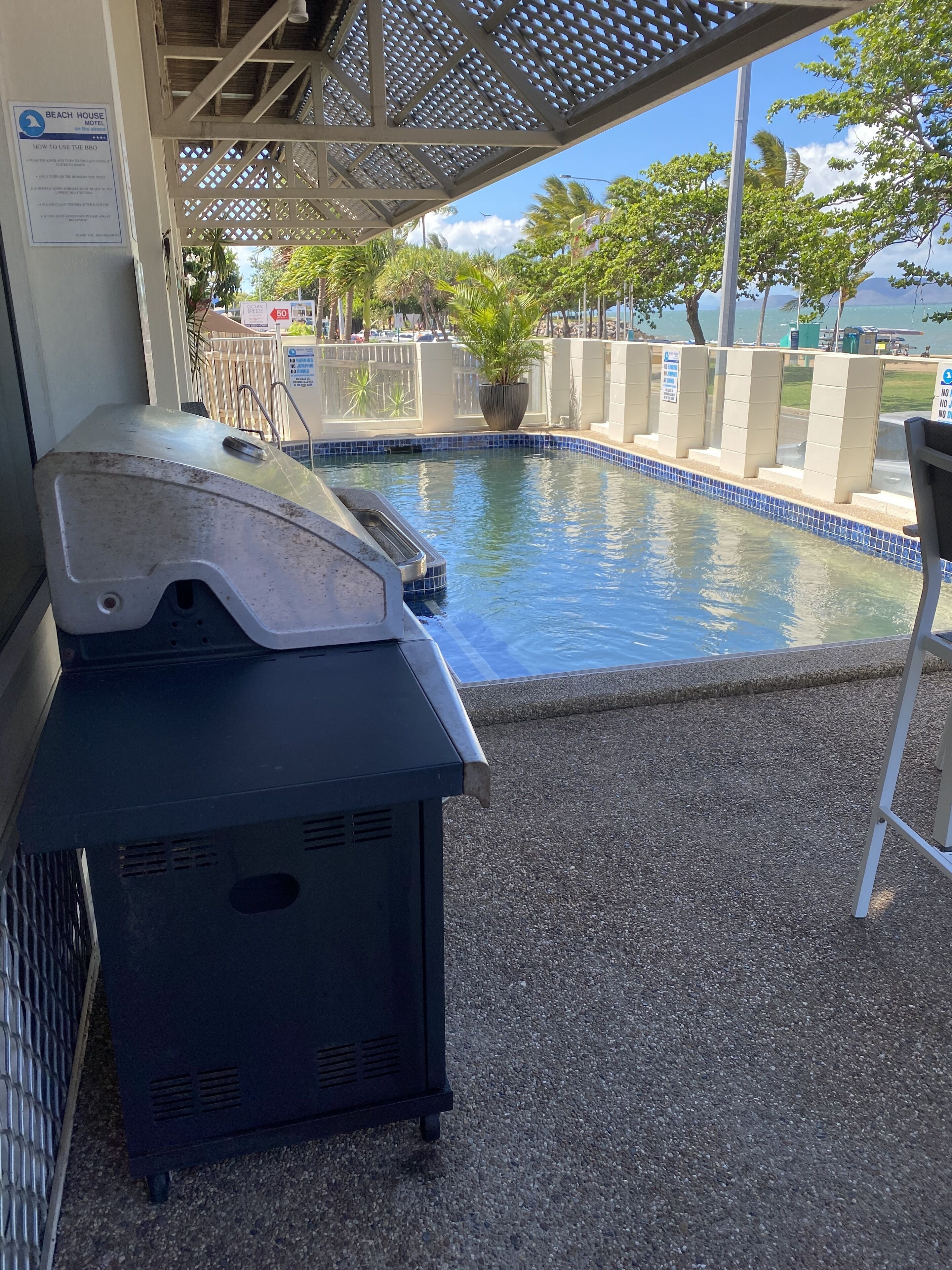 Zona de piscina con una parrilla y un letrero sobre el uso de la barbacoa.