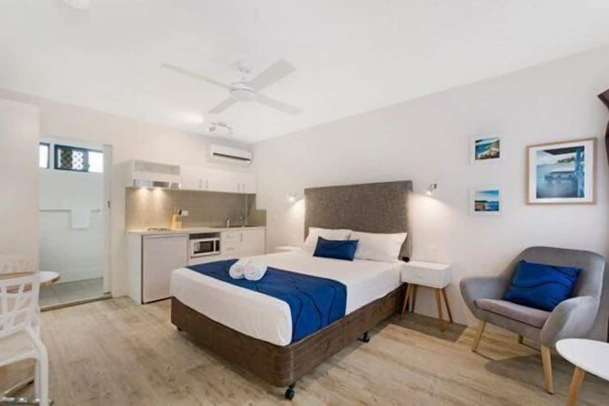 Une chambre d’hôtel moderne équipée d’un lit, d’une table de chevet, d’une chaise et d’une kitchenette.
