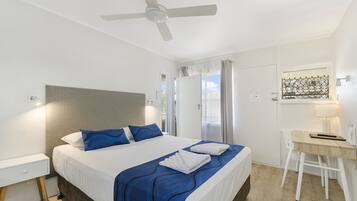 A modern hotel room with a large bed, a desk, and a ceiling fan.