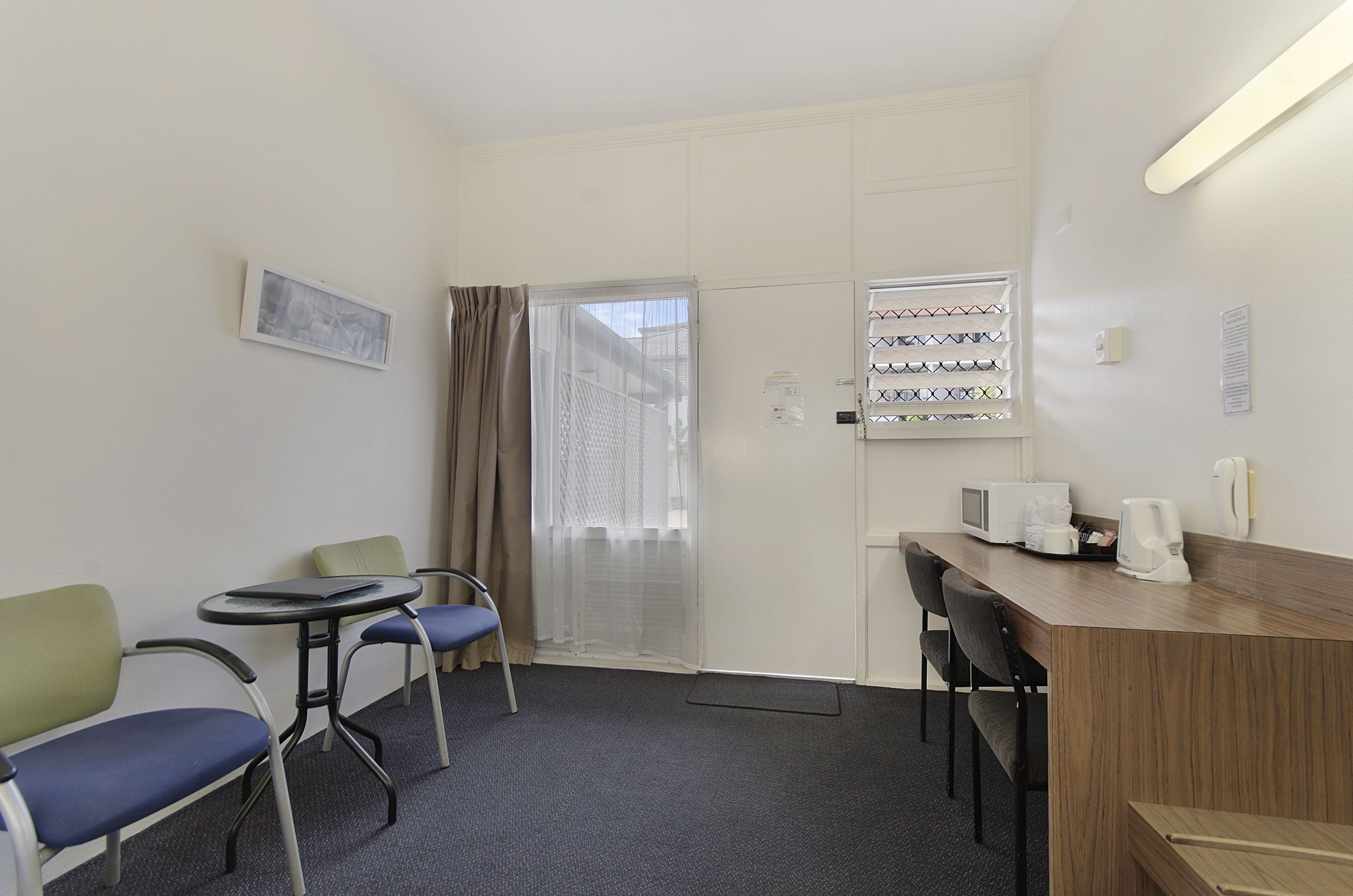 A hotel room with a wooden desk, two chairs, a small table, a microwave, and a coffee maker.