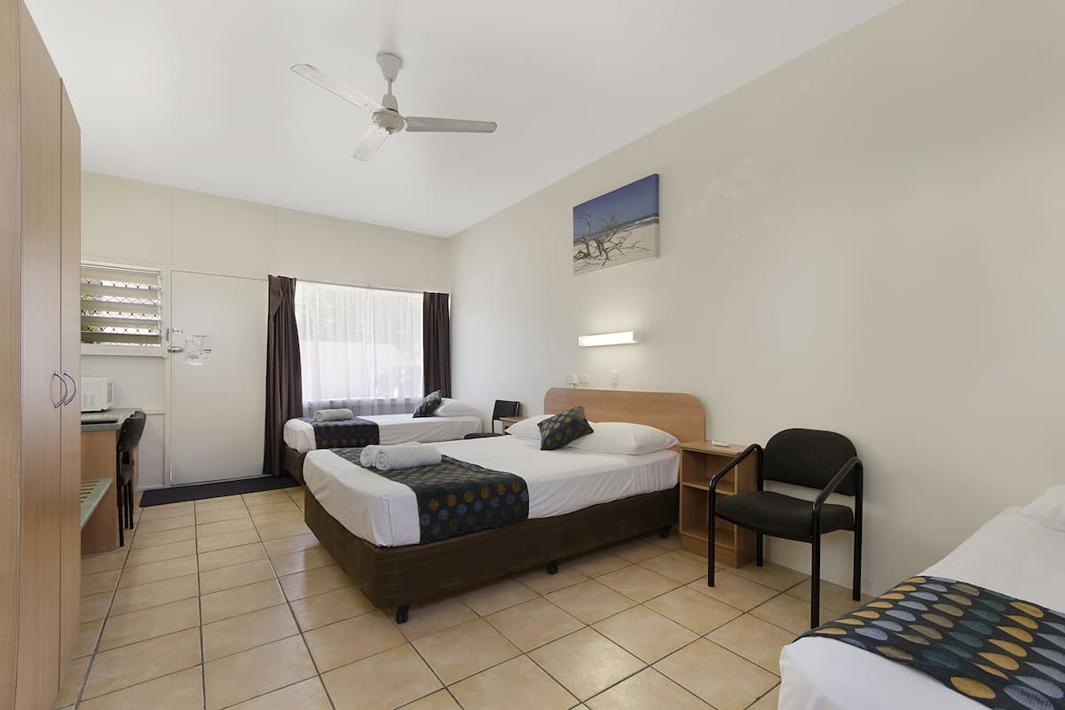 Une chambre d’hôtel avec deux lits, un bureau, une chaise, un ventilateur de plafond et un tableau au mur.