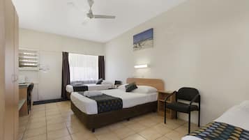 Ein Hotelzimmer mit zwei Betten, einem Schreibtisch, einem Stuhl, einem Deckenventilator und einem Bild an der Wand.