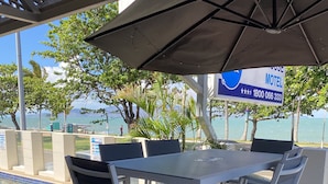 A covered outdoor seating area with a pool view, a sign for a motel, and a clear sky. - Beach House Motel (North Ward)