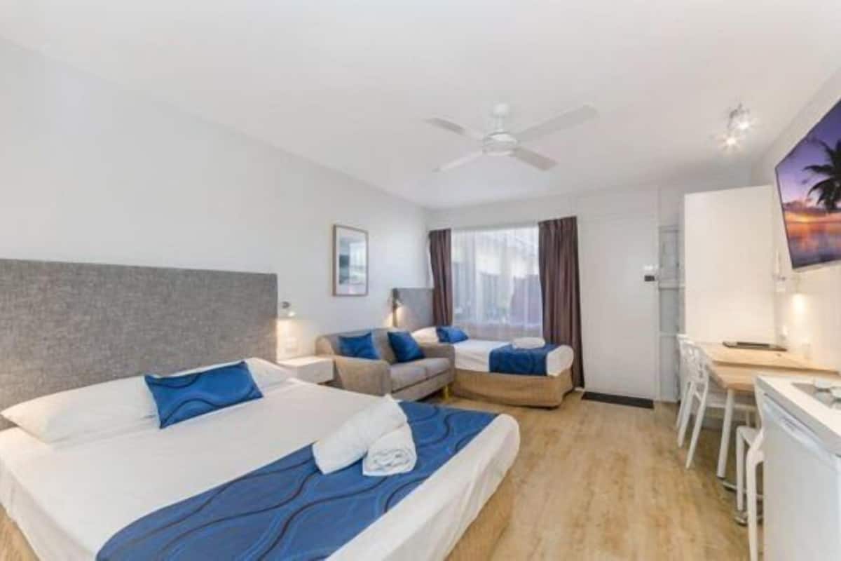 Une chambre d’hôtel avec deux lits, un bureau, une chaise, un ventilateur de plafond et un tableau au mur.