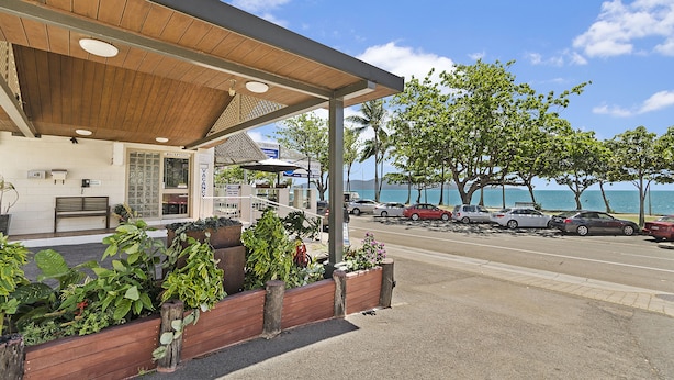 A beachfront hotel with a covered outdoor seating area, a reception desk, and a view of the ocean. - Beach House Motel (North Ward)