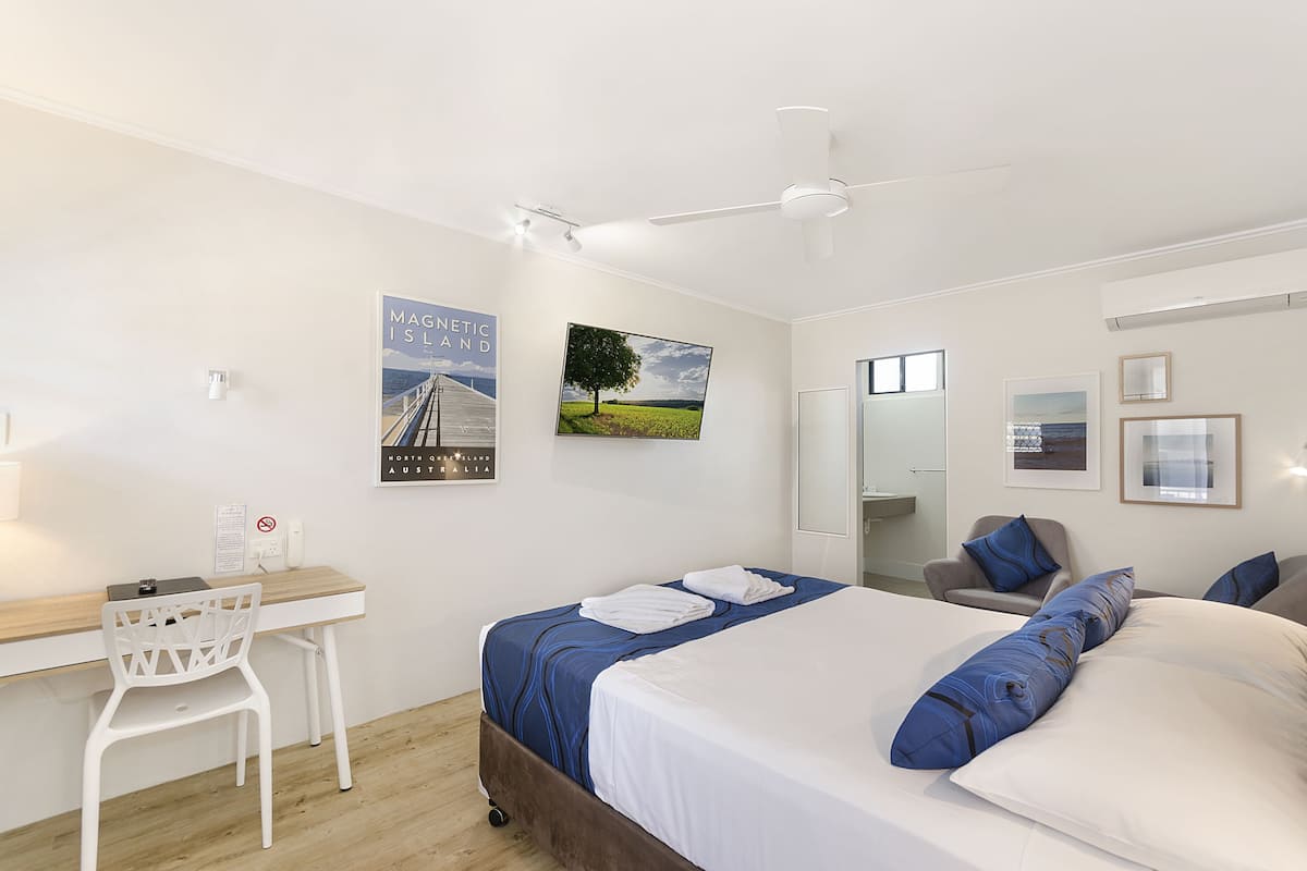Une chambre d’hôtel moderne, équipée d’un lit, d’un bureau et d’une chaise. Les murs sont ornés de posters et le plafond est doté d’un ventilateur.