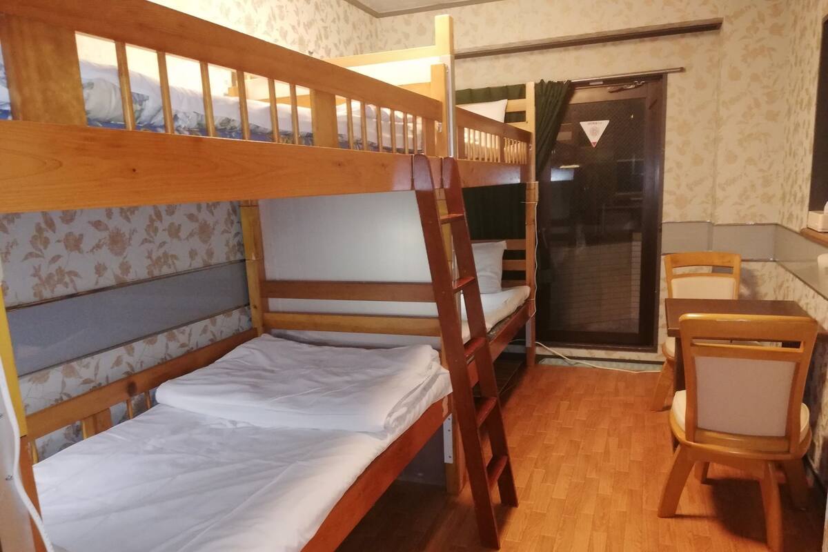 A bunk bed room with a desk and chair, wooden flooring, and a window with a view.