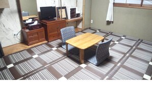 A room with a wooden table and two patterned chairs, a TV on a stand, and a cabinet with drawers. - Family & bAKpAK Tokyo Hostel (Tokyo)