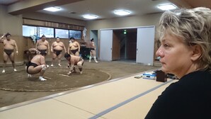 A sumo wrestling practice area with wrestlers in traditional attire, a tatami mat, and a spectator. - Family & bAKpAK Tokyo Hostel (Tokyo)
