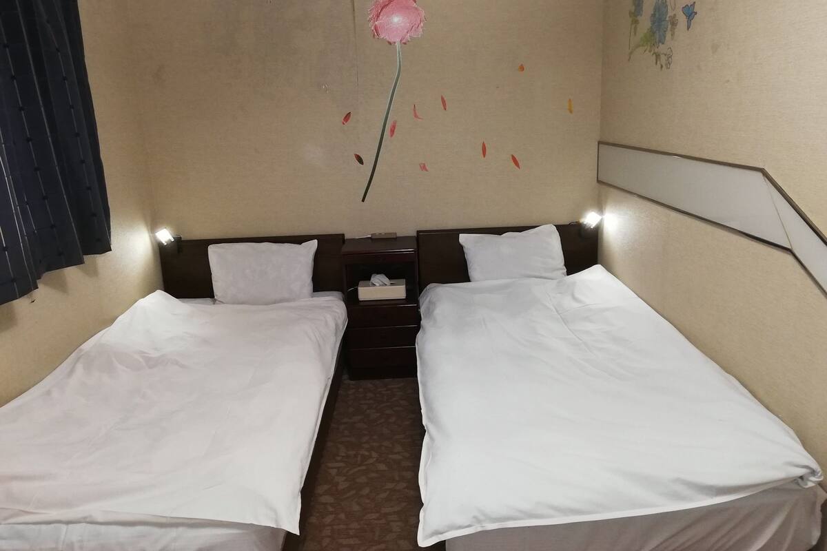 A hotel room with two single beds, a nightstand with a lamp, and a wall decoration of a flower.