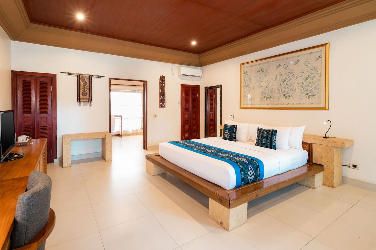 A spacious bedroom with a large bed, wooden furniture, and a view of the outside.