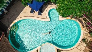 An aerial view of a swimming pool with a unique shape, surrounded by lounge chairs and a small hot tub. - Villa Almarik (Gili Trawangan)