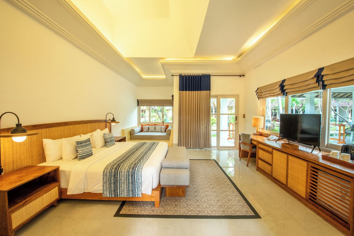 A spacious hotel room with a large bed, a sofa, a TV, and a wooden cabinet.