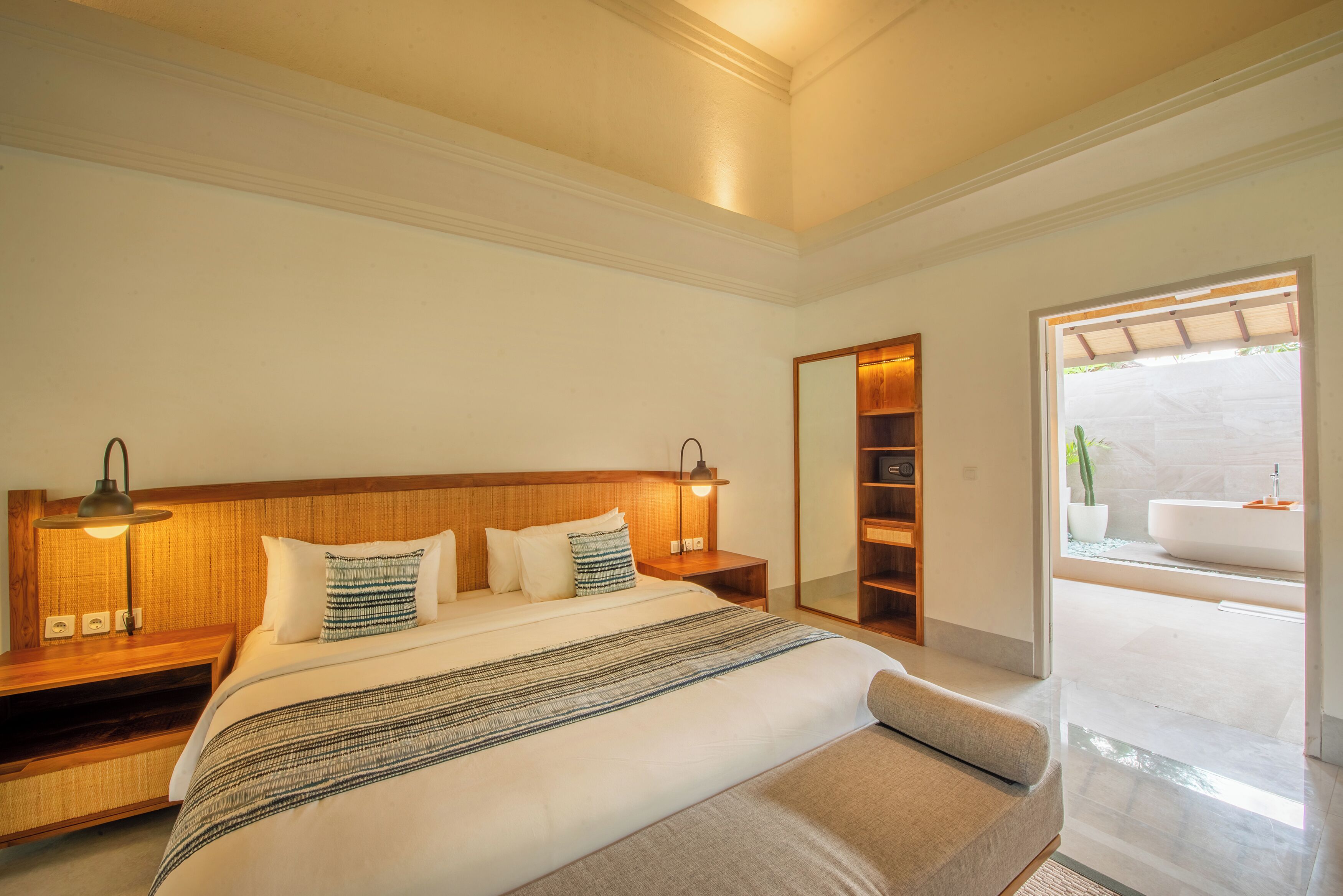 A modern hotel room with a large bed, bedside tables, a mirror, and a view of the bathroom.