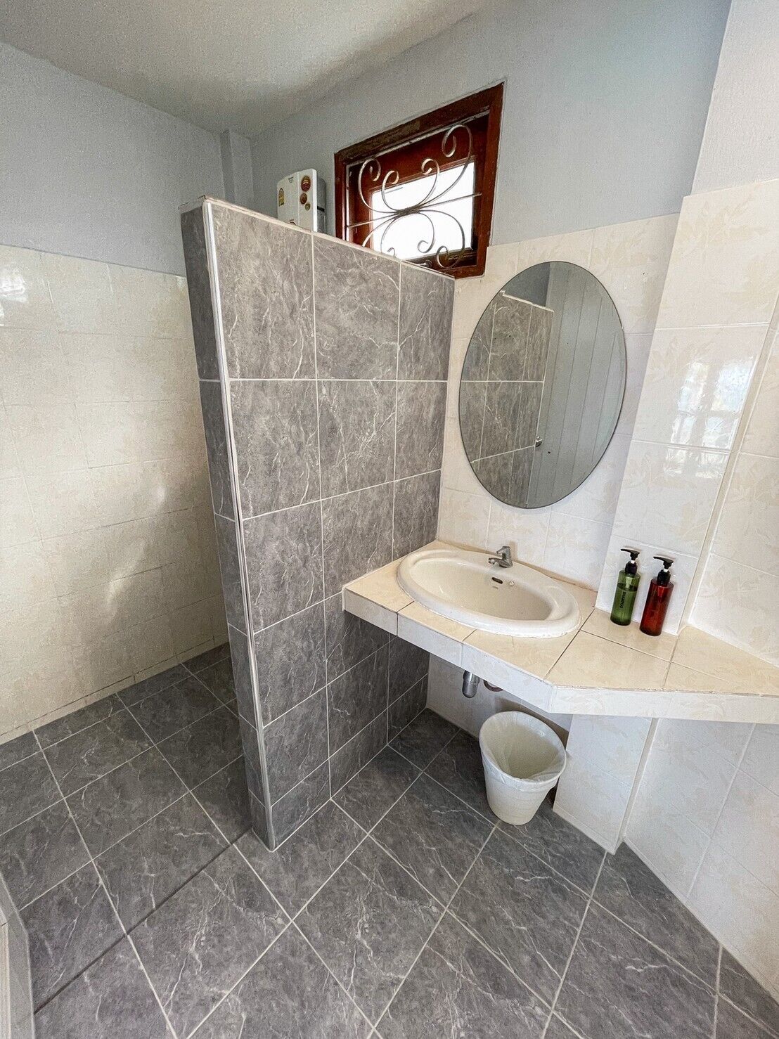 A bathroom with a shower, a sink, a mirror, and a window with decorative ironwork.