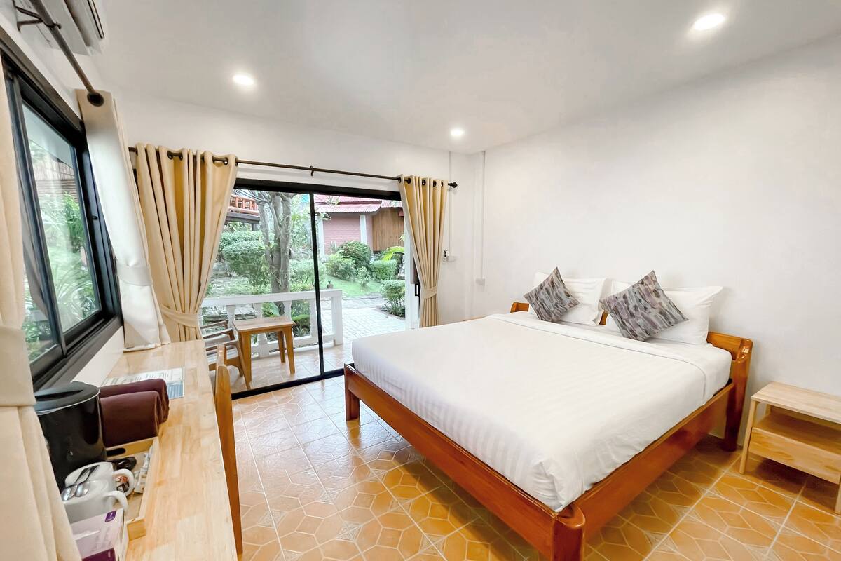 Un dormitorio con una cama grande, un escritorio y vistas a un jardín a través de una puerta corrediza de vidrio.