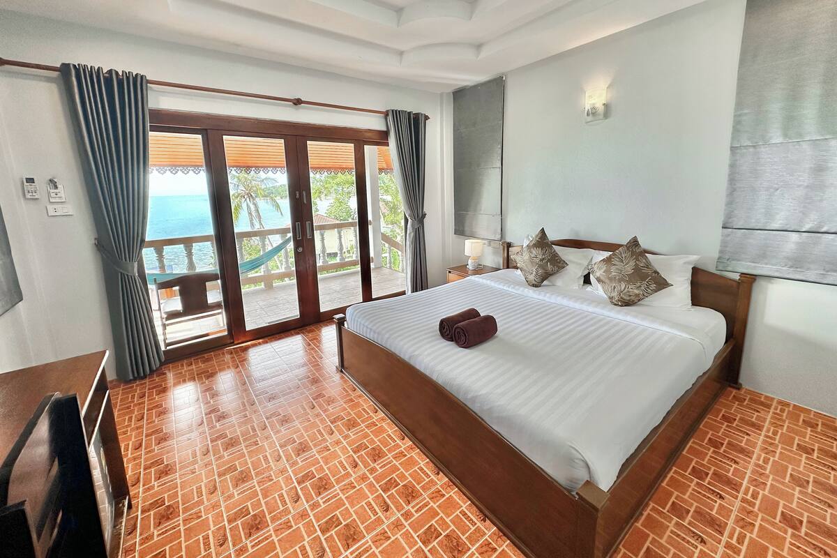 Una habitación de hotel con una cama grande, un escritorio y vistas al mar a través de puertas correderas.
