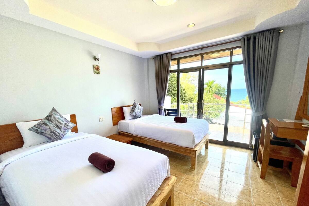 Habitación de hotel con dos camas, un escritorio y vista al océano.