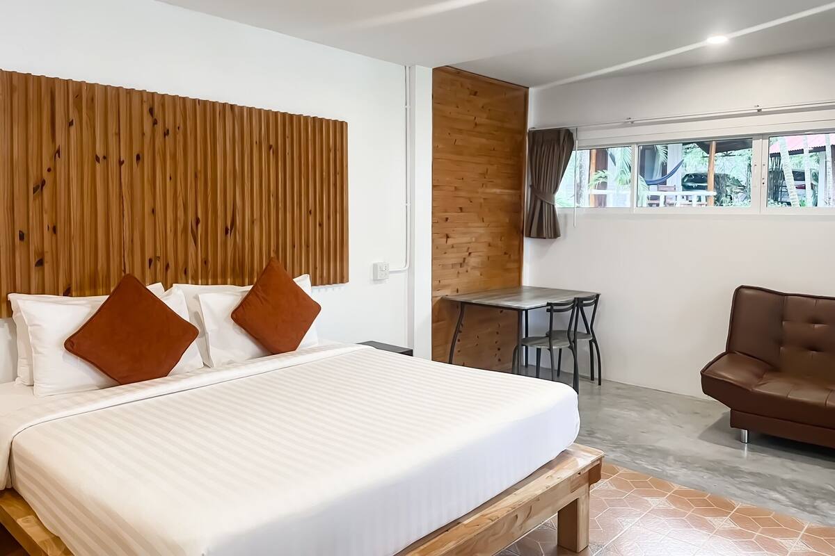 Una habitación de hotel moderna con una cama grande, un cabecero de madera, un escritorio pequeño y un sofá de cuero marrón.