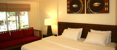 A hotel room with a bed, a red sofa, a nightstand with a lamp, and two wall art pieces.