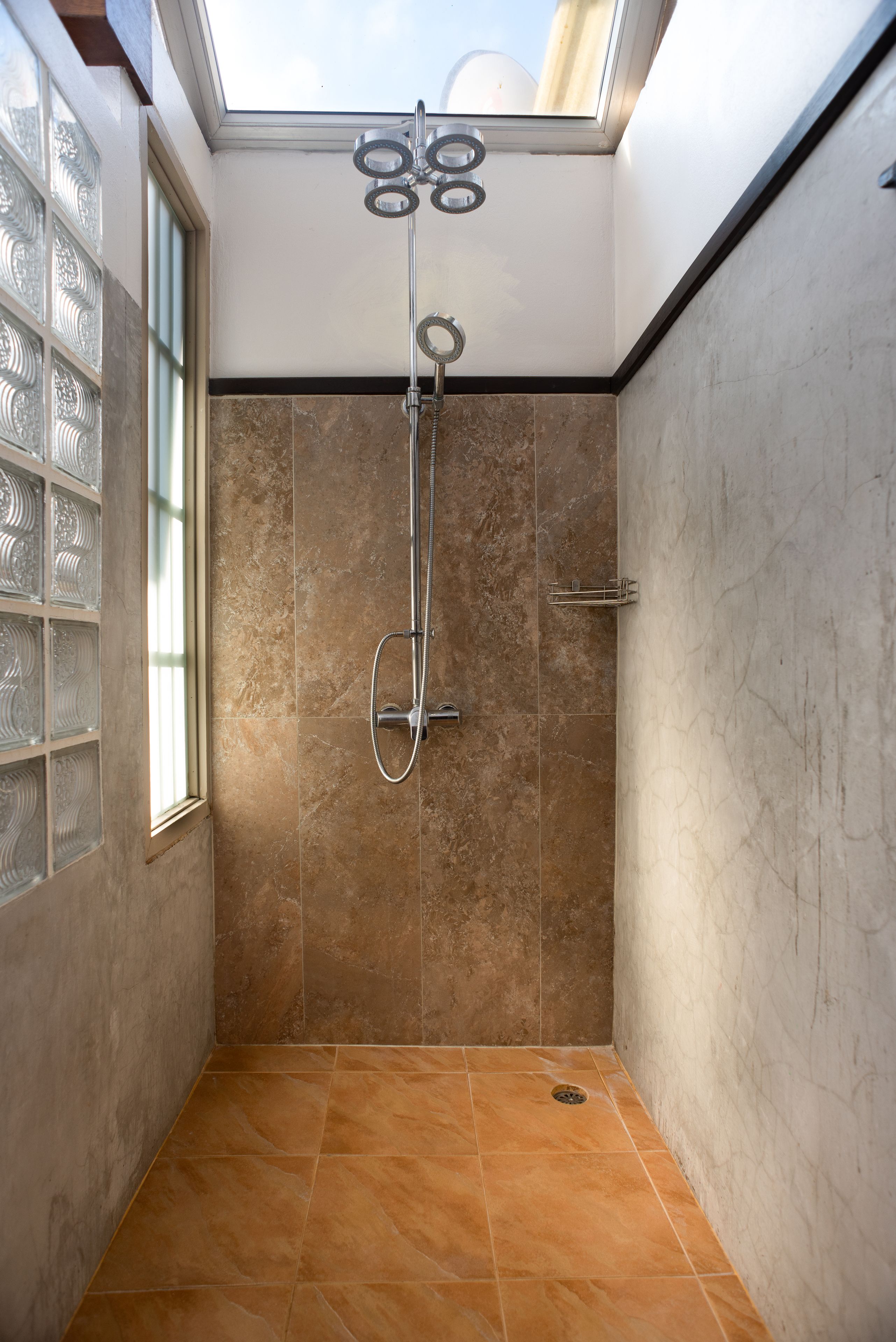 A shower with a glass door, a skylight, and a tiled floor.