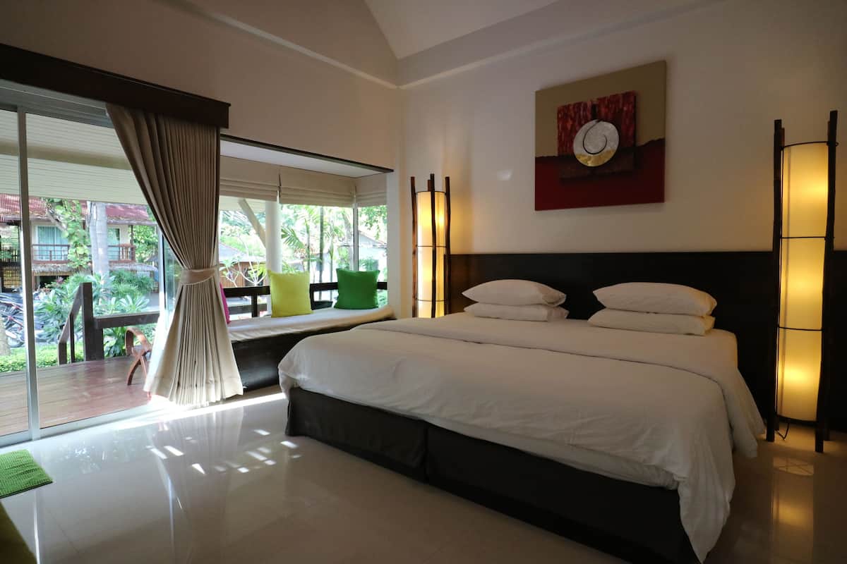 A modern hotel room with a large bed, a window with curtains, a view of the outside, and a painting on the wall.