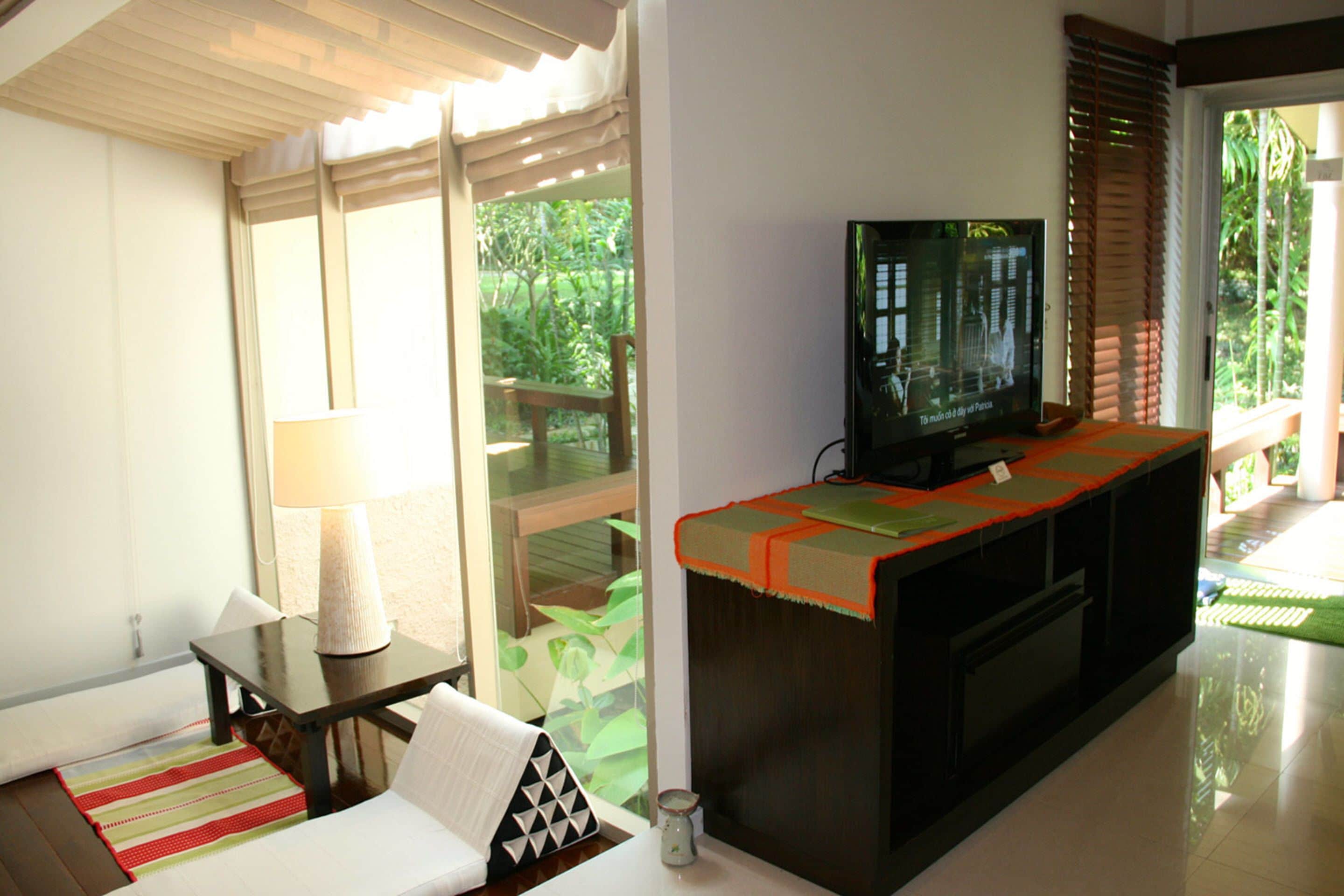 A living room with a television, a sofa, a table, and a window overlooking a garden.