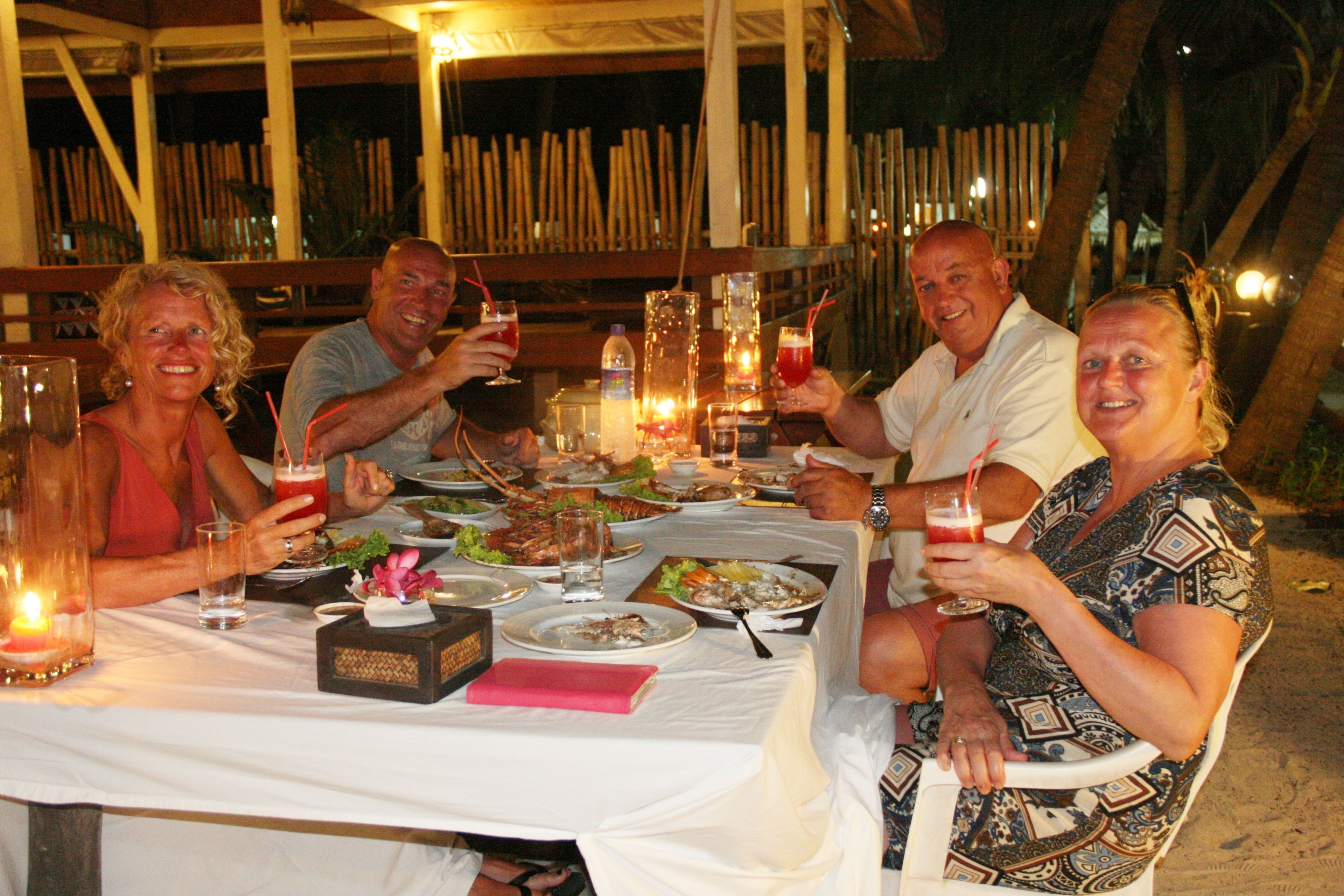 A group of people dining at an outdoor table with candles, drinks, and various dishes.