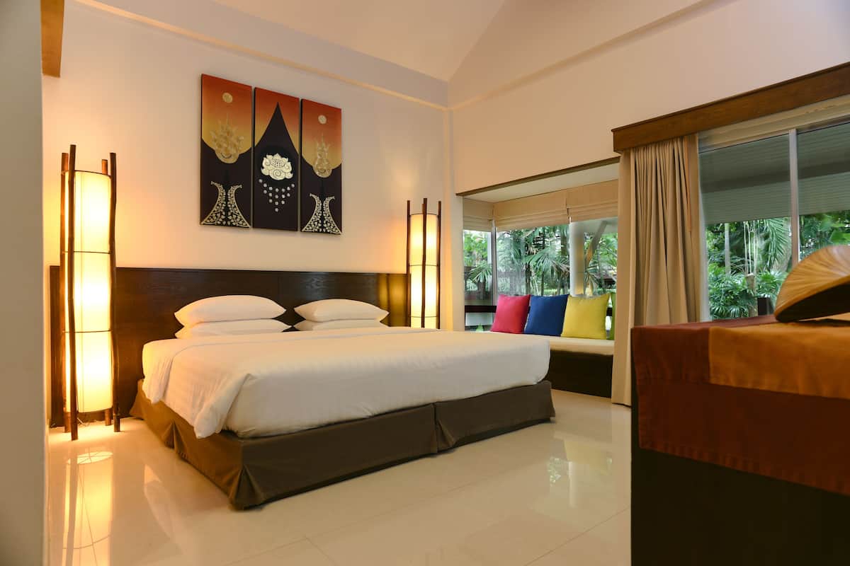 A hotel room with a large bed, a nightstand, a lamp, and a window with curtains.