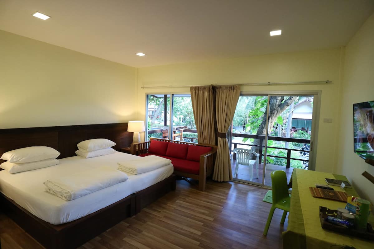 A hotel room with a large bed, a red sofa, a dining table, and a view of the outdoors.