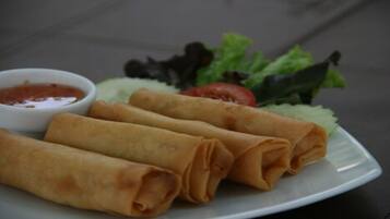 Un plato de rollitos primavera con salsa para mojar y una ensalada pequeña.