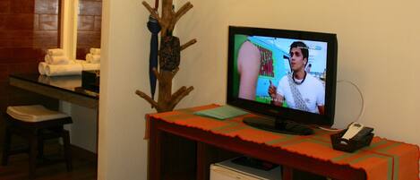 A small living room with a television, a wooden coat rack, a small refrigerator, and a wooden bench.