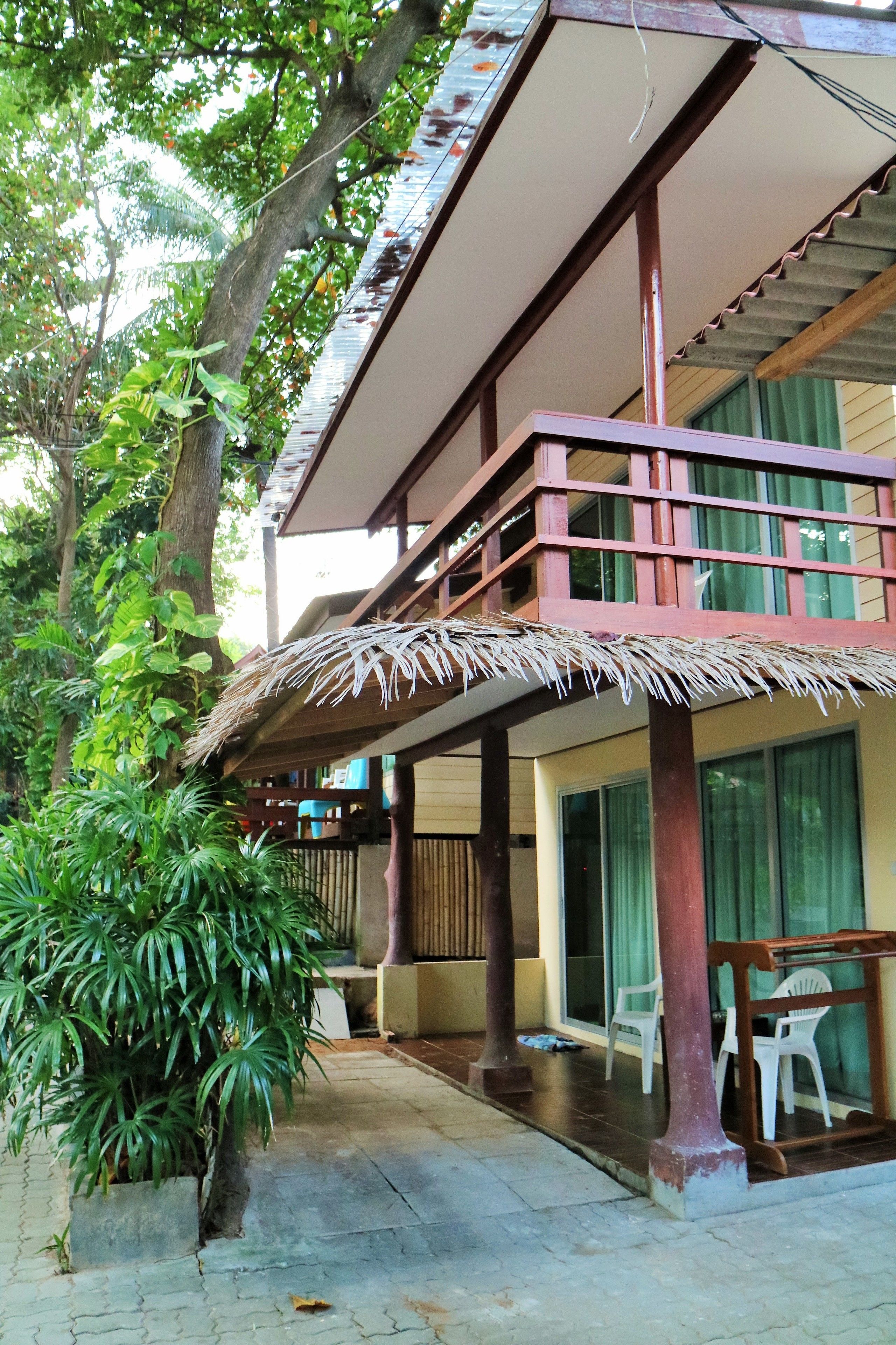 A two-story building with a thatched roof balcony, large windows, and a potted plant.