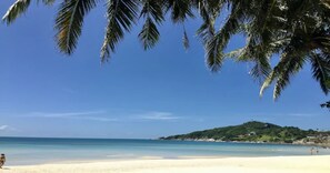 Une plage avec un ciel dégagé, des palmiers et une colline qui se dessine à l’horizon.